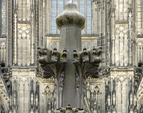 Final Detailreiche gotische Kreuzblume vor der beeindruckenden Fassade des Kölner Doms.Detailed Gothic finial in front of the impressive façade of Cologne Cathedral.