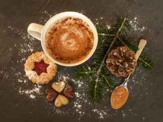 Bad Driburg - Hot Chocolate Eine Tasse heiße Schokolade, umgeben von Weihnachtsgebäck und Tannenzweigen auf dunklem Untergrund.