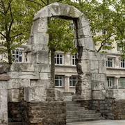 Römertorbogen Restaurierter Torbogen aus der römischen Antike in Köln, umrahmt von Bäumen, vor modernem Gebäude.Restored archway from Roman antiquity in Cologne, framed by trees, in front of a modern building.