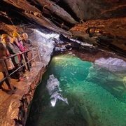 Führung im Besucherbergwerk "Marie Louise Stolln" Vier Personen mit gelben Helmen stehen auf einem Geländer in einer beleuchteten Höhle mit grünem Wasser, die Atmosphäre ist abenteuerlich.