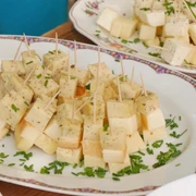 Würfel aus Käse mit Kräutern und Zahnstochern, angerichtet auf einem Teller mit feiner Verzierung.