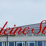 LiebedeineStadt Gebäude mit rotem Schriftzug „Liebe deine Stadt“ auf dem Dach, bewölkter Himmel im Hintergrund.Building with red lettering “'Liebe deine Stadt”' on the roof, cloudy sky in the background.
