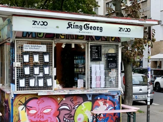 King Georg Kiosk Farbenfroher Kiosk „King Georg Büdchen“ mit Graffiti, Speisekarten und Getränkeschildern an der Glasscheibe.Colorful "King Georg Büdchen" kiosk with graffiti, menus and drinks signs on the glass.