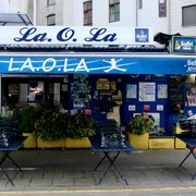 La Ola Büdchen Kiosk "La.O.La" in Köln, mit blauer Fassade und Gaffel-Logo markanten Sitzmöglichkeiten vor dem Eingang.Kiosk "La.O.La" in Cologne, with blue façade and Gaffel logo, striking seating in front of the entrance.