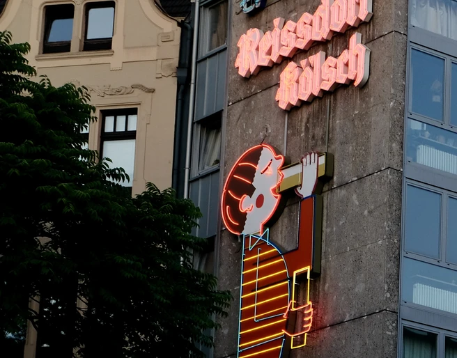 Reissdorf neon sign Neonreklame am Kölner Gebäude zeigt das ikonische Reissdorf-Kölsch-Logo, umgeben von Architektur.Neon advertising on the Cologne building shows the iconic Reissdorf-Kölsch logo, surrounded by architecture.