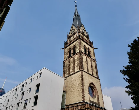 Christ Church Turm der Christuskirche in Köln bei klarem Himmel, links modernere Gebäude, im Hintergrund ein Sendeturm.Tower of the Christuskirche in Cologne with clear skies, modern buildings on the left, and a transmission tower in the background.