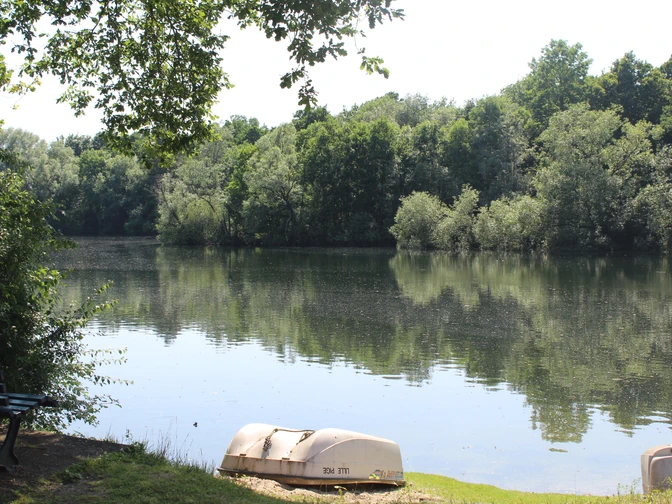 Ein ruhiger See mit umgebenden Bäumen und zwei kleinen Booten im Vordergrund bietet eine friedliche Naturkulisse.