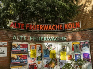 Alte Feuerwache Die Alte Feuerwache Köln mit einer Ziegelmauer voller bunter Plakate und einem leuchtenden Schriftzug oben.The old fire station in Cologne with a brick wall full of colorful posters and a bright lettering at the top.
