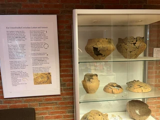 Vitrine mit antiken Keramikgefäßen, die teilweise rekonstruiert sind, in einem Ausstellungsraum.