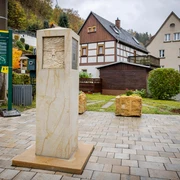 Caspar-David-Friedrich-Stele Steinsäule mit Relief auf gepflastertem Platz, umgeben von Fachwerkhäusern und Infotafel; herbstliche Stimmung.
