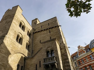 Eigelsteintorburg Die Eigelsteintorburg in Köln ist ein imposantes, historisches Bauwerk aus Sandstein. Auf dem Bild ist die massive Fassade mit ihren markanten Bögen und Türmen zu sehen, die in den blauen Himmel ragen. Rechts im Vordergrund steht ein Baum, dessen Blätter einen Kontrast zur Architektur bilden. Im Hintergrund sind bunte Hausfassaden zu erkennen, die einen urbanen Kontext hinzufügen.The Eigelsteintorburg in Cologne is an imposing, historic building made of sandstone. The picture shows the massive façade with its striking arches and towers rising into the blue sky. On the right in the foreground is a tree whose leaves form a contrast to the architecture. In the background, colorful house facades can be seen, adding an urban context.