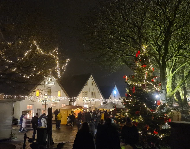 Weihnachtsmarkt Greetsiel Zu sehen ist der Blick auf den Weihnachtsmarkt bei Dunkelheit und mit Lichterketten. Vorne steht eine große geschmückte Weihnachtstanne.