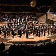 Berliner Philharmoniker Das Bild zeigt die Berliner Philharmoniker in einem modernen Saal, umgeben von einem aufmerksamen Publikum.