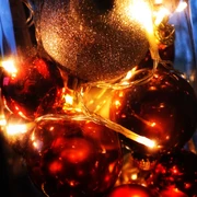 weihnachten.jpg Leuchtende Weihnachtskugeln, gold und rot, in Nahaufnahme mit warmen Lichterketten umgeben.