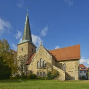 Sankt Laurentius in Bissendorf Historische Kirche mit spitzem Turm und rotem Dach, umgeben von Bäumen unter blauem Himmel.