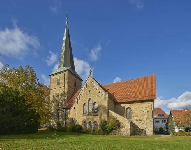 Sankt Laurentius in Bissendorf Historische Kirche mit spitzem Turm und rotem Dach, umgeben von Bäumen unter blauem Himmel.