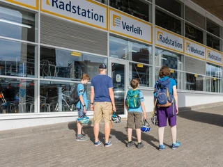 Cologne bike station Familie vor der Radstation in Köln mit Fahrradhelmen blickt auf Fahrräder hinter großen Fenstern.Family in front of the bike station in Cologne with bicycle helmets looking at bicycles behind large windows.