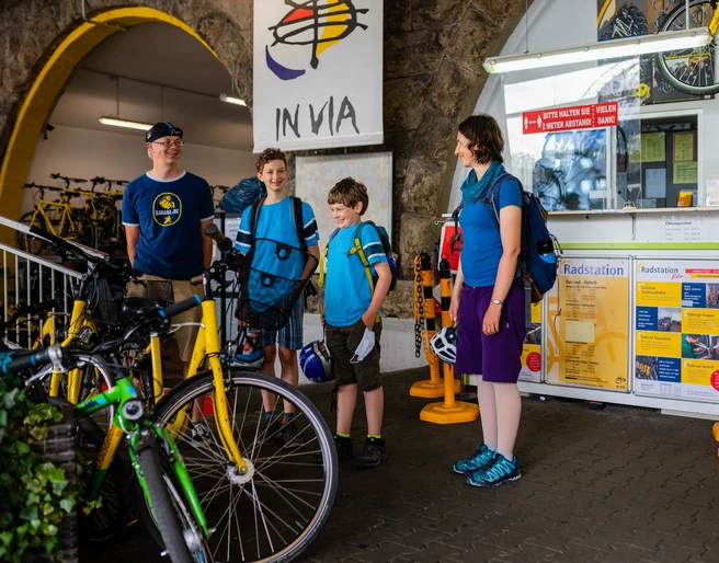 Cologne bike station Vier Personen in Freizeitkleidung, mit Fahrrädern vor einem Informationsschalter.Four people in casual clothes, with bicycles in front of an information desk.