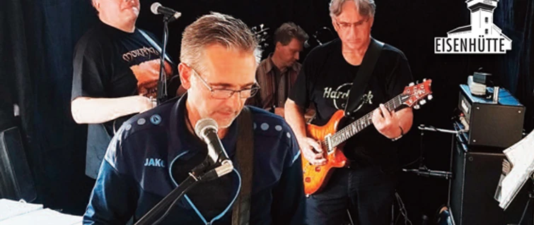 TUSH 2024.jpg Band spielt live auf Bühne der Eisenhütte, Musiker mit Gitarren und Mikrofon in konzentrierter Stimmung.