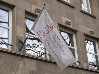 Belgian House RGM Das Bild zeigt eine elegante, cremefarbene Flagge vor der Fassade eines Gebäudes mit der Aufschrift "Römisch-Germanisches Museum im Belgischen Haus Köln". The picture shows an elegant, cream-colored flag in front of the facade of a building with the inscription "Römisch-Germanisches Museum im Belgischen Haus Köln".
