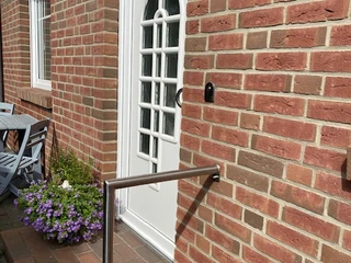 Brauer, Liebenau  Eingangstür eines Backsteinhauses mit weißer Tür, Blumenbeet und Handlauf auf der linken Seite.