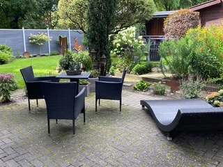 Gepflegte Terrasse mit modernen Rattanmöbeln, umgeben von blühenden Pflanzen und begrünten Büschen.