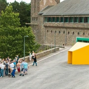 Personengruppe steht vor modernem, gelbem Kunstwerk, historische Burg Vogelsang im Hintergrund.