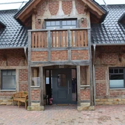 Rotes Backsteingebäude mit Fachwerkdetails und einem Balkon, umgeben von gepflasterten Flächen.