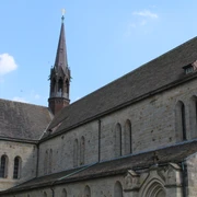 Gotisches Klostergebäude mit imposantem Kirchturm aus rotem Backstein vor klarem, blauem Himmel.
