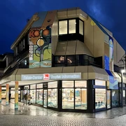 Tourist Information Paderborn, Außenansicht Tourist Information Paderborn mit leuchtendem Eingang in moderner Architektur bei Dämmerung.