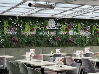 Ein lichtdurchfluteter Wintergarten mit vertikaler Pflanzendekoration und Sitzgelegenheiten im Café.