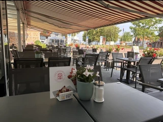Geschützte Terrasse mit blühenden Blumen und einladender Atmosphäre, Tische und Stühle unter Markisen.