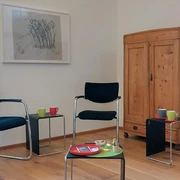Feierabend_Dialog 2023_perspektiv katrinbusch_smt.jpg Meetingraum mit Holzboden, mehreren schwarzen Stühlen, einem Schrank und Flipchart, bereit für Diskussionen.