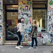 Belgian Quarter Zwei Personen betrachten eine mit Stickern und Graffiti verzierte Wand in einer Stadtstraße.Two people look at a wall decorated with stickers and graffiti in a city street.