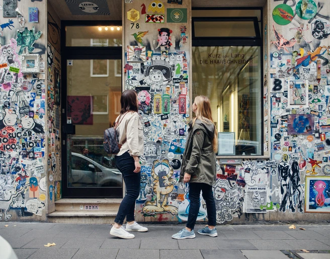 Belgian Quarter Zwei Personen betrachten eine mit Stickern und Graffiti verzierte Wand in einer Stadtstraße.Two people look at a wall decorated with stickers and graffiti in a city street.