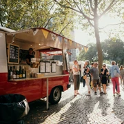 meet & eat Cologne Ein farbenfroher Foodtruck auf einem sonnigen Platz, umgeben von Menschen, die in entspannter Atmosphäre Essen genießen.A colorful food truck in a sunny square, surrounded by people enjoying food in a relaxed atmosphere.