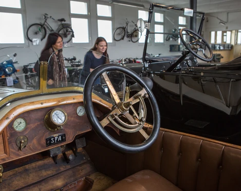 Automuseum Melle Im Automuseum Melle sind historische Autos in einem hellen Raum ausgestellt. Menschen betrachten die Fahrzeuge.