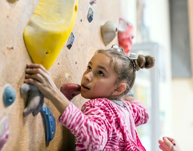 Junior Climber hanging on holds on climbing wall Junior Climber hanging on holds on climbing wall