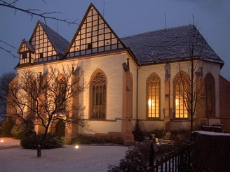 Beleuchtete Klosterkirche in Blomberg bei Dämmerung mit schneebedecktem Dach und gotischen Fenstern.