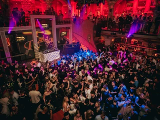 Alando Palais(c)next-choice 4.jpg Menschen tanzen in einem belebten, farbenfroh beleuchteten Nachtclub mit DJ auf einer erhöhten Bühne.People dance in a lively, colorfully lit nightclub with a DJ on a raised stage.Mensen dansen in een levendige, kleurrijk verlichte nachtclub met een DJ op een verhoogd podium.