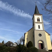 ev. Bartholomäuskirche  <p>Gelbe Kirche mit Glockenturm in Lohmar vor blauem Himmel und umliegender Natur.</p>