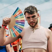 Cologne Pride Ein junger Mann in einem ärmellosen Oberteil posiert selbstbewusst mit einem bunten Fächer.A young man in a sleeveless top poses confidently with a colorful fan.