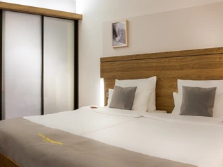 Doppelzimmer Standard Zweibettzimmer mit Holzdekor, weißen Bettwäsche und zwei grauen Kissen, gemütlich beleuchtet.Twin room with wooden decor, white bed linen and two gray pillows, cozy lighting.