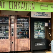 Lebensmittelautomat in FArchant 2-türiger Kühlschrank mit verschiedenen regionalen Lebensmitteln sowie ein  Maschine für Softeis, darüber steht auf grünem Banner : 24 Stunden einkaufen zu bezahlen in bar und mit Karte