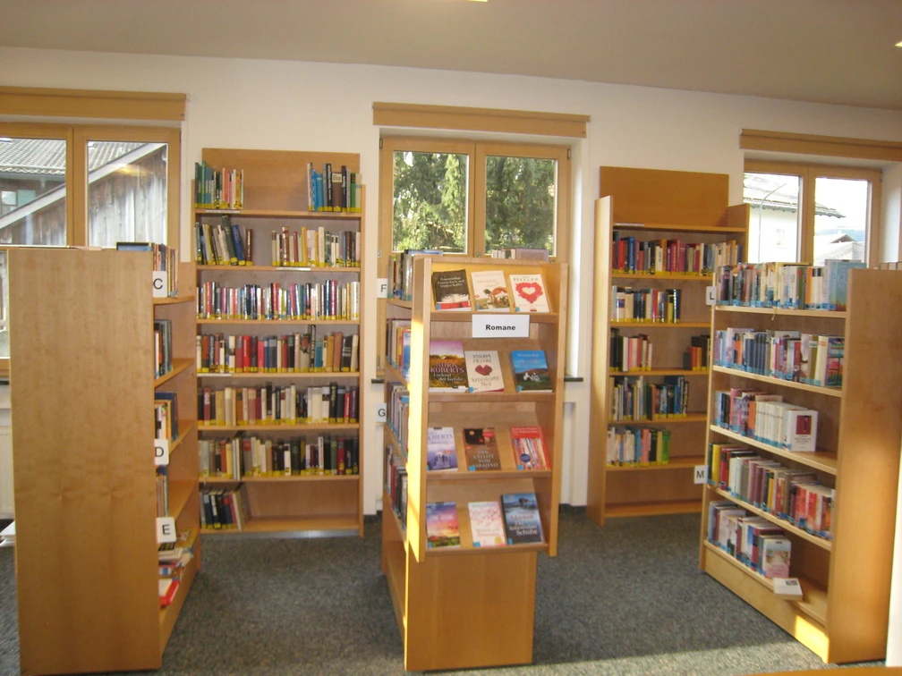 Gemeindebücherei Farchant Stehschränke mit verschiedenen Büchern, im Hintergrund Wandregale mit Büchern sowie 3 Fenster mit Rollos
