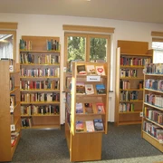 Gemeindebücherei Farchant Stehschränke mit verschiedenen Büchern, im Hintergrund Wandregale mit Büchern sowie 3 Fenster mit Rollos
