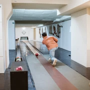 Kegeln im Brauhaus Koelsche Boor (13).jpg Eine Person in Jeans und orangefarbener Jacke spielt Kegeln in einem Innenraum mit Holzboden.</p>A person in jeans and an orange jacket plays skittles in an indoor room with a wooden floor.</p> <p