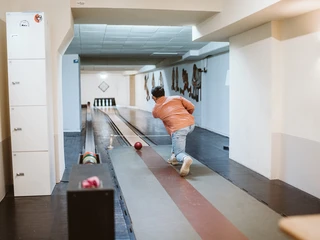 Kegeln im Brauhaus Koelsche Boor (13).jpg Eine Person in Jeans und orangefarbener Jacke spielt Kegeln in einem Innenraum mit Holzboden.</p>A person in jeans and an orange jacket plays skittles in an indoor room with a wooden floor.</p> <p