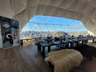 Island Landschaft Innenraum eines geodätischen Kuppelzeltes mit gedeckten Tischen und Bergblick durch große Fenster.Interior of a geodesic dome tent with covered tables and mountain views through large windows.