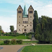 Abdinghofkirche in Paderborn vor blauem Himmel, umgeben von grünen Rasenflächen und Bäumen.